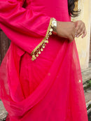 A close-up of a bright pink traditional outfit with a sheer dupatta and a gold coin-trimmed sleeve, worn by a model.